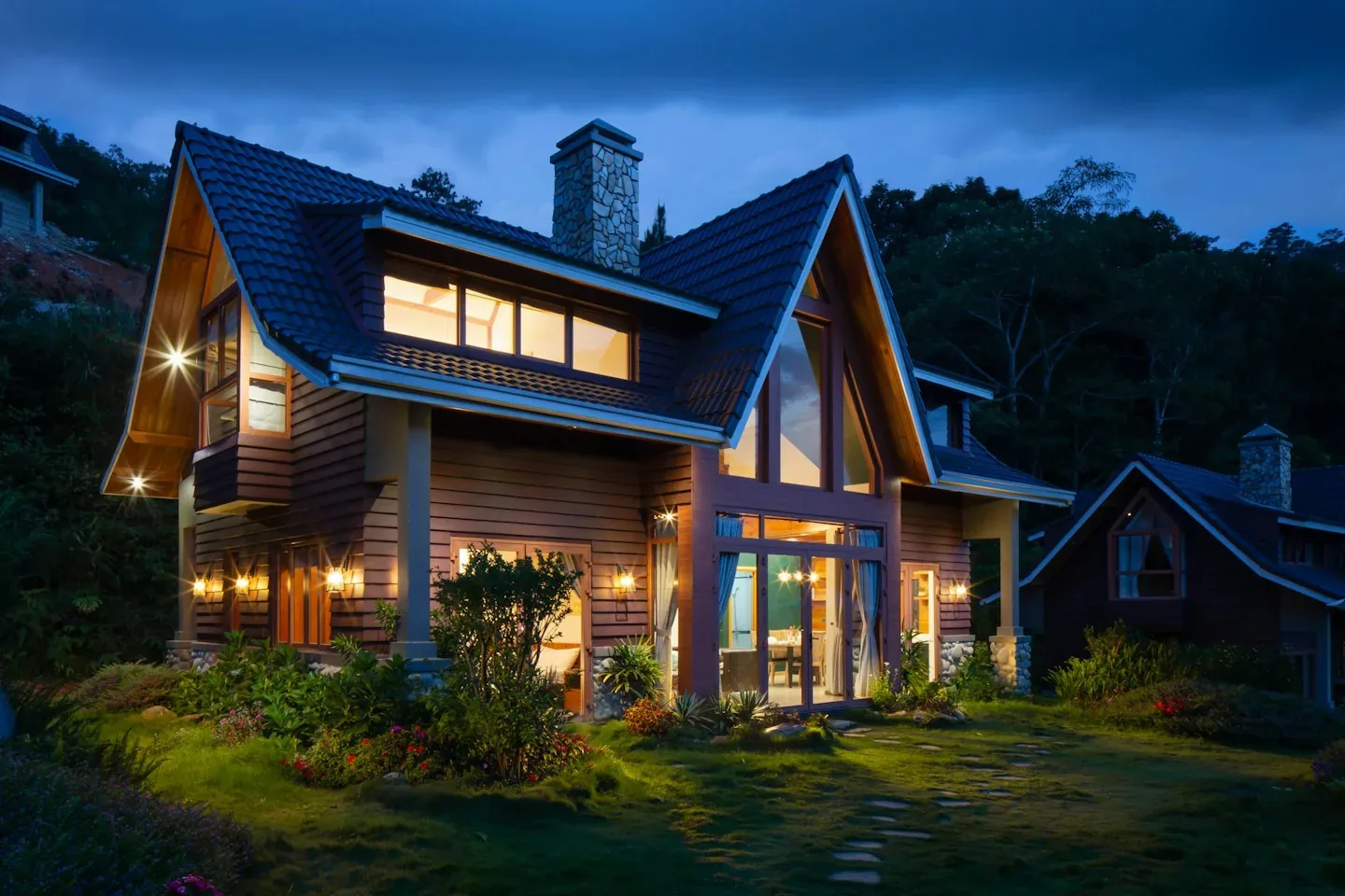 A warmly lit home with a front porch and landscaped garden at dusk